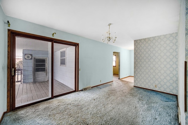 spare room with wallpapered walls, visible vents, an accent wall, an inviting chandelier, and carpet flooring