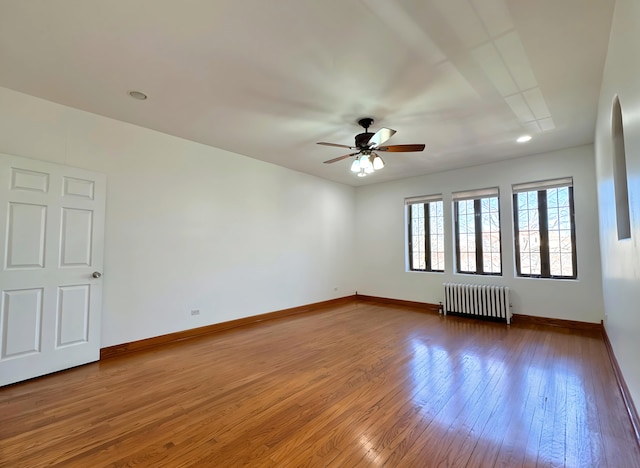 empty room featuring baseboards, hardwood / wood-style floors, and radiator heating unit