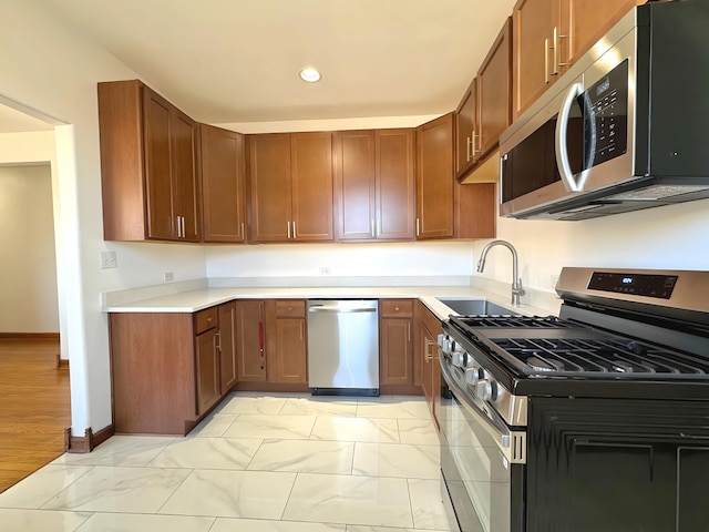 kitchen featuring baseboards, stainless steel appliances, light countertops, a sink, and recessed lighting