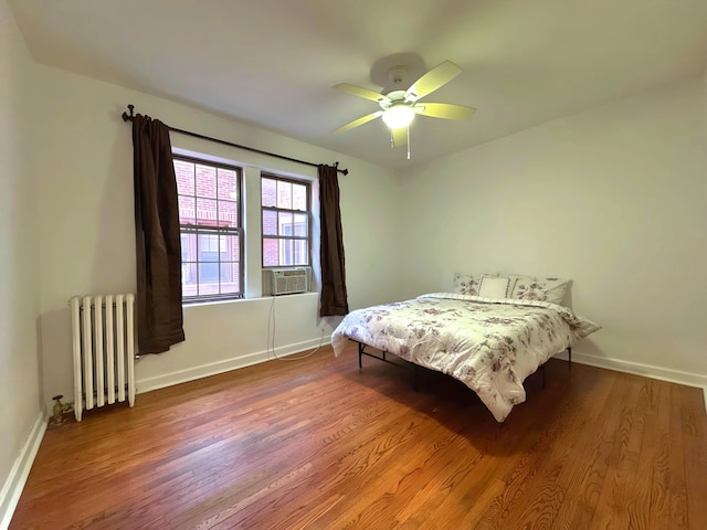 bedroom with radiator heating unit, a ceiling fan, wood finished floors, cooling unit, and baseboards