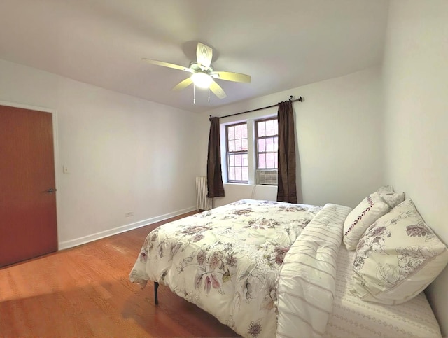 bedroom with radiator, a ceiling fan, wood finished floors, cooling unit, and baseboards