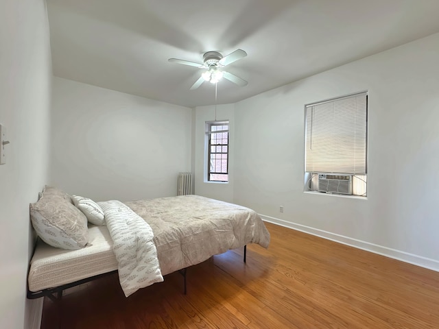 bedroom featuring baseboards, a ceiling fan, radiator, wood finished floors, and cooling unit