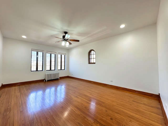 unfurnished room featuring baseboards, wood-type flooring, a ceiling fan, and radiator