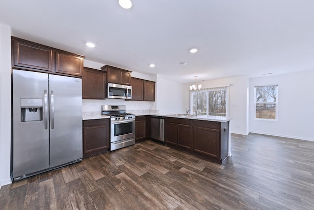 kitchen featuring dark wood finished floors, stainless steel appliances, a sink, dark brown cabinets, and a peninsula