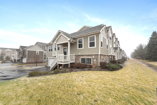 view of front of property featuring aphalt driveway, a front yard, stone siding, and an attached garage