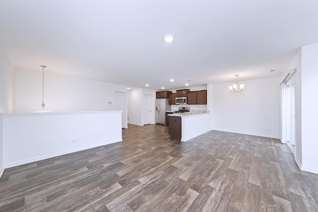 unfurnished living room featuring recessed lighting, dark wood finished floors, baseboards, and an inviting chandelier