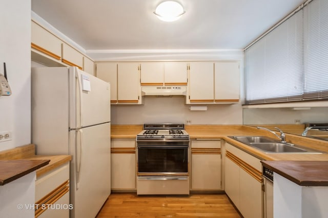 kitchen with light wood finished floors, under cabinet range hood, gas range, freestanding refrigerator, and a sink