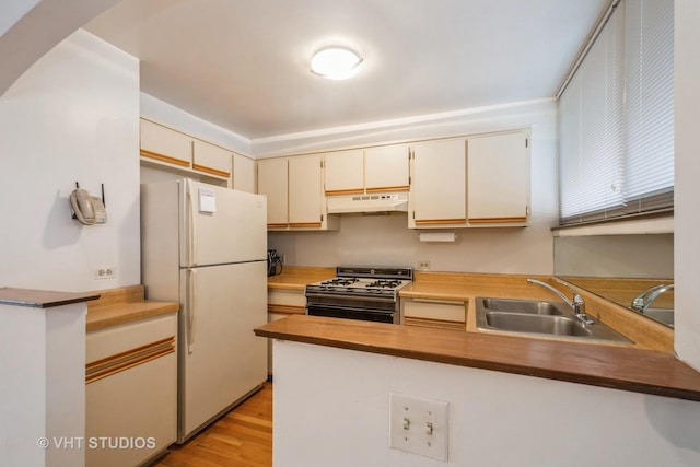 kitchen featuring under cabinet range hood, a sink, freestanding refrigerator, range with gas cooktop, and a peninsula