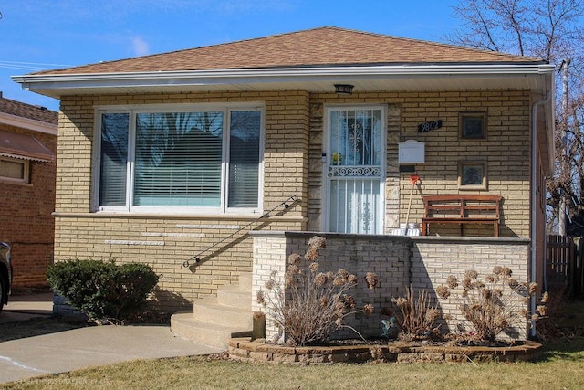 bungalow-style home featuring brick siding and roof with shingles