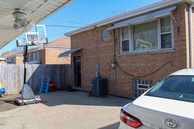 view of side of property featuring fence, central AC unit, a patio, and brick siding