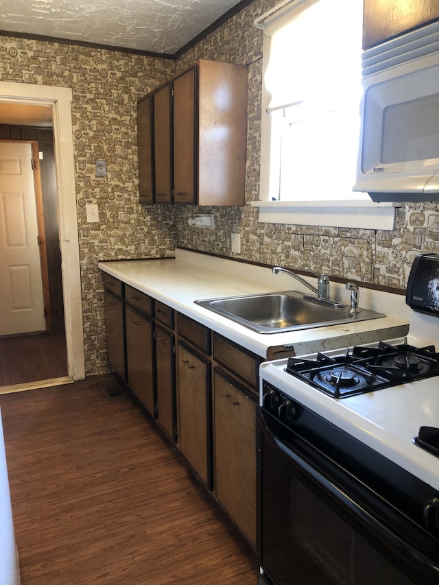 kitchen featuring dark wood finished floors, light countertops, white microwave, a sink, and gas range