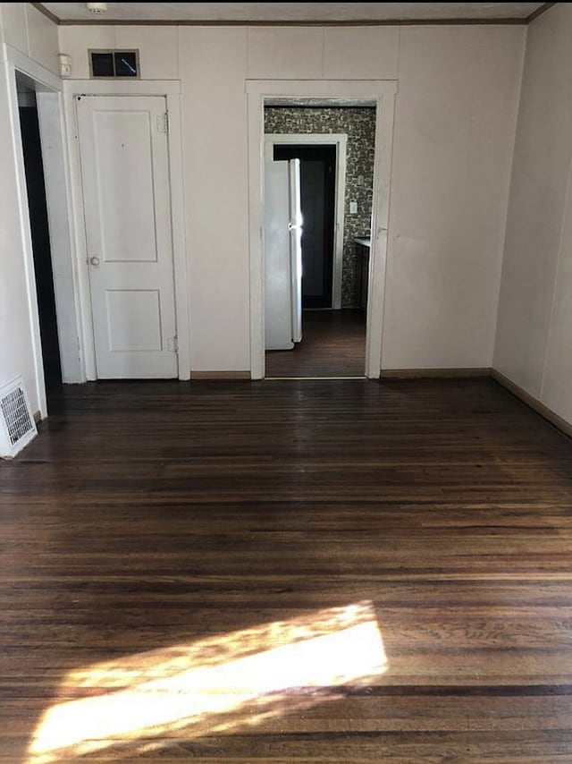 spare room featuring baseboards, visible vents, and dark wood finished floors