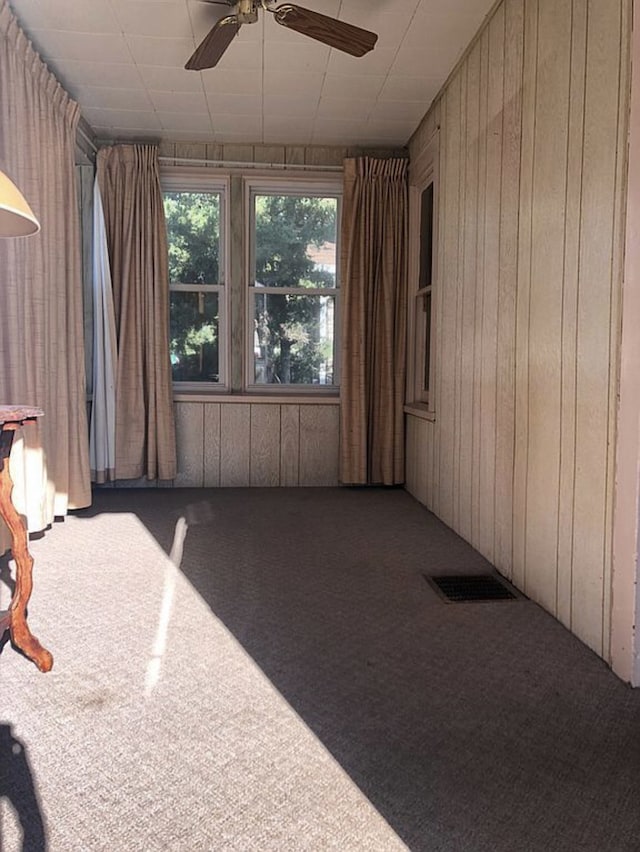 spare room featuring visible vents, carpet floors, a ceiling fan, and wooden walls