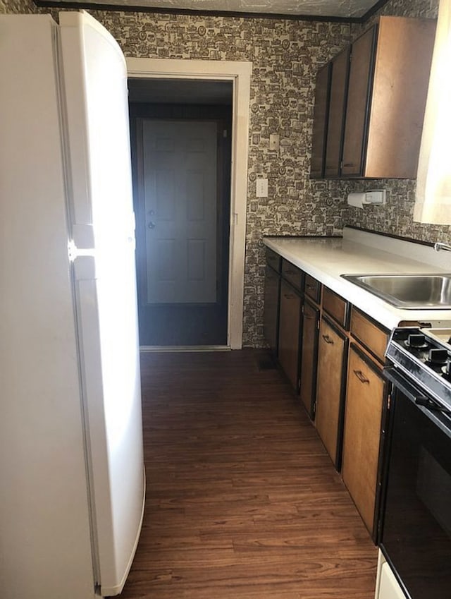 kitchen with dark wood-style floors, freestanding refrigerator, light countertops, a sink, and gas stove