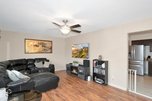 living area featuring a ceiling fan, baseboards, and wood finished floors