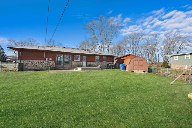 rear view of property with a storage shed, stone siding, fence, and a lawn