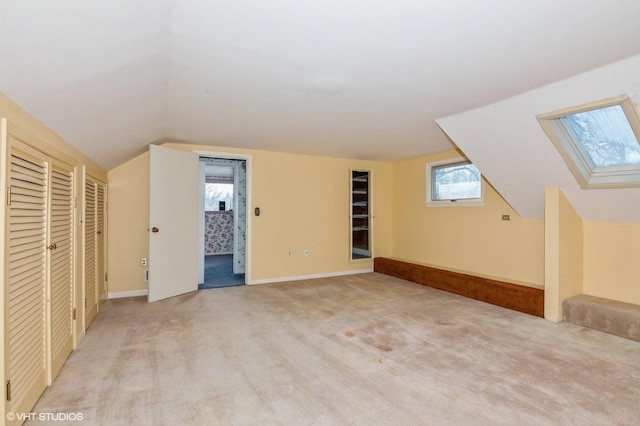 additional living space featuring baseboards, vaulted ceiling with skylight, and light carpet