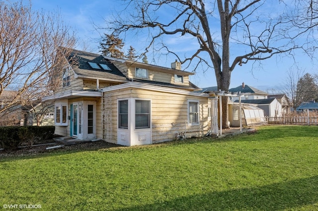 back of property with a yard, solar panels, a chimney, and fence