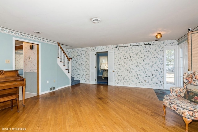 living area with visible vents, hardwood / wood-style floors, stairway, wallpapered walls, and baseboards