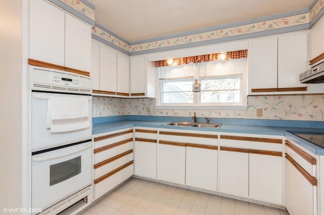 kitchen featuring wallpapered walls, a sink, light countertops, white cabinetry, and double oven