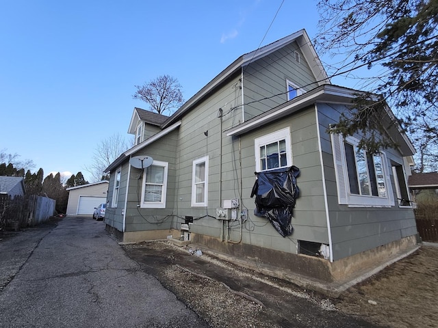 view of property exterior with a detached garage, fence, and an outbuilding