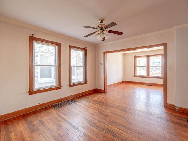 spare room with visible vents, ceiling fan, baseboards, ornamental molding, and light wood-style flooring