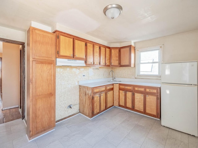 kitchen with under cabinet range hood, light countertops, freestanding refrigerator, and a sink