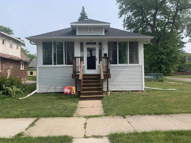 bungalow-style house featuring covered porch, a shingled roof, a sunroom, and a front yard