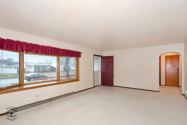 spare room with arched walkways, light carpet, and baseboards