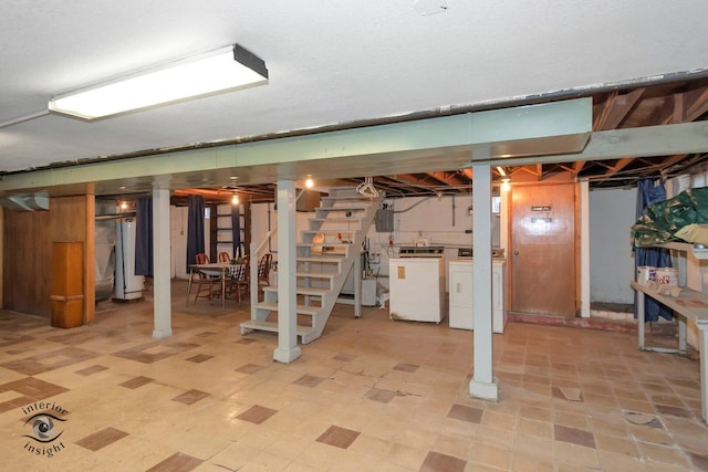 unfinished below grade area featuring light floors, electric panel, stairway, and washer and clothes dryer