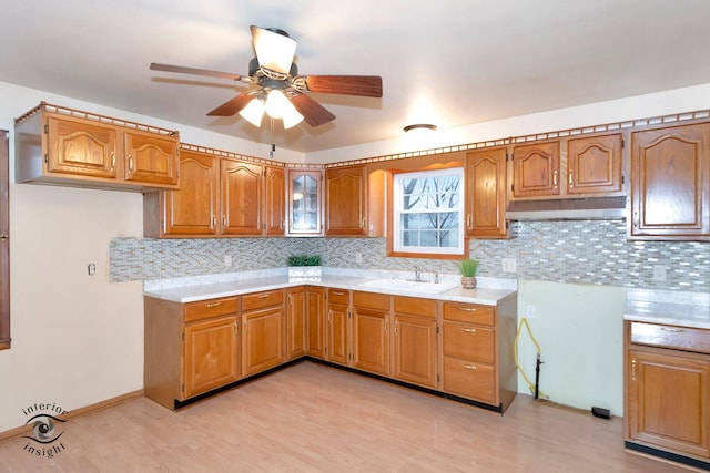 kitchen with light countertops, brown cabinets, a sink, and under cabinet range hood