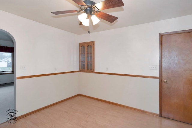 spare room featuring arched walkways, baseboards, ceiling fan, and light wood finished floors