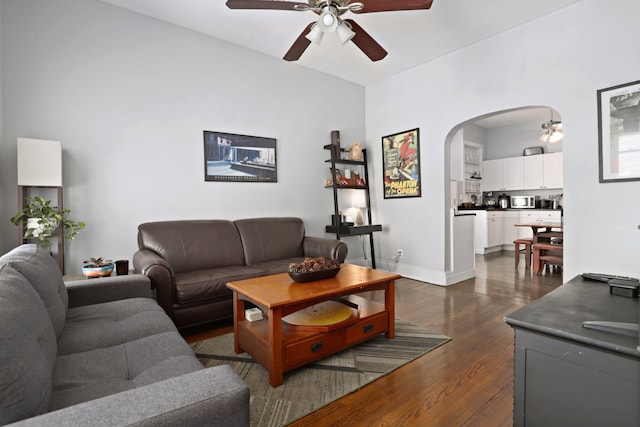 living room with a ceiling fan, arched walkways, dark wood-style flooring, and baseboards