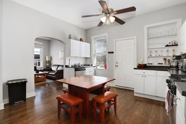 dining area featuring arched walkways, dark wood finished floors, a ceiling fan, and a wealth of natural light