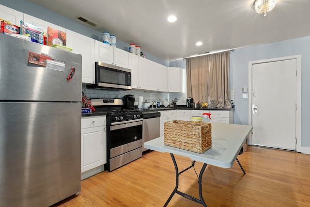 kitchen featuring decorative backsplash, white cabinets, stainless steel appliances, and light wood-style floors