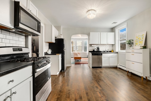 kitchen with dark countertops, dark wood finished floors, white cabinetry, arched walkways, and appliances with stainless steel finishes