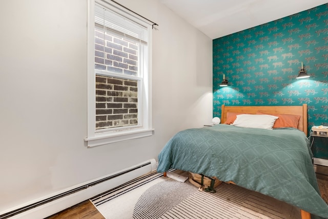 bedroom with a baseboard heating unit, wood finished floors, wallpapered walls, and an accent wall