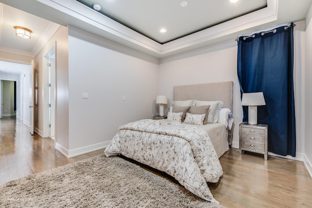 bedroom with ornamental molding, a tray ceiling, wood finished floors, and baseboards