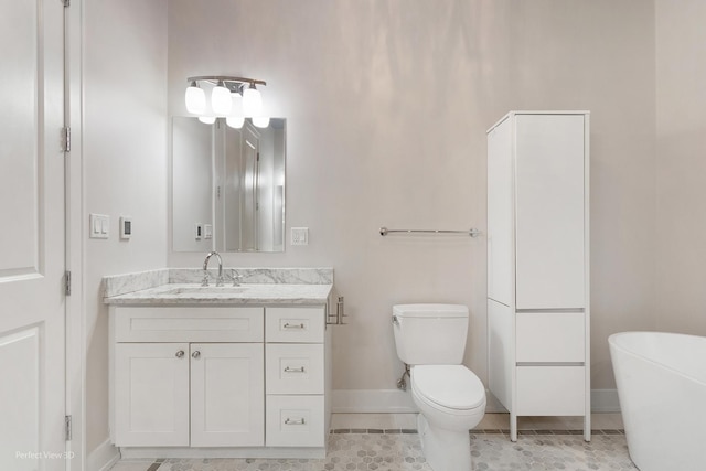 bathroom featuring tile patterned flooring, toilet, a freestanding tub, vanity, and baseboards