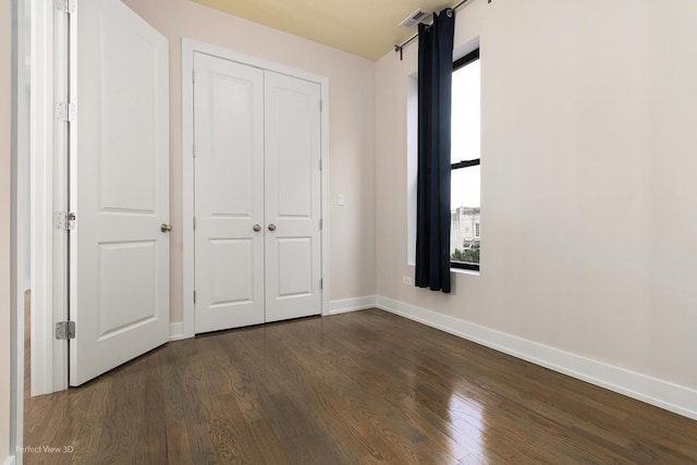 unfurnished bedroom featuring dark wood-type flooring, a closet, visible vents, and baseboards