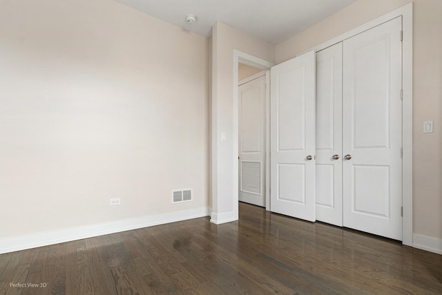 unfurnished bedroom featuring dark wood-style floors, a closet, visible vents, and baseboards