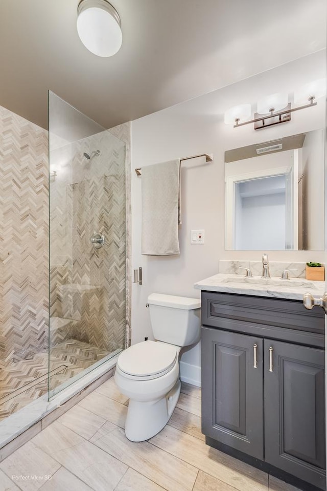 full bath with visible vents, a tile shower, vanity, and toilet