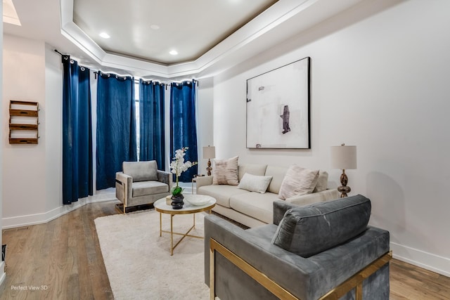 living room featuring light wood finished floors, baseboards, a raised ceiling, and recessed lighting