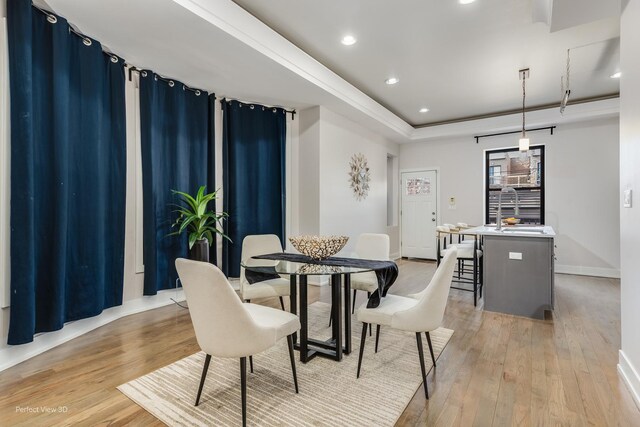 dining room with light wood-style floors, recessed lighting, a tray ceiling, and baseboards