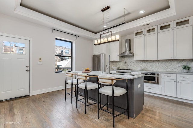 kitchen featuring a kitchen breakfast bar, wall chimney exhaust hood, a raised ceiling, and stainless steel appliances