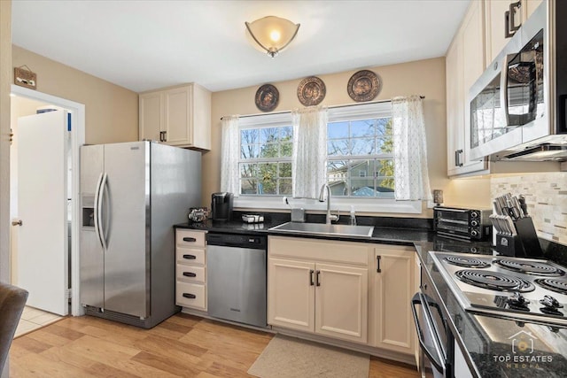 kitchen with a sink, dark countertops, backsplash, stainless steel appliances, and light wood-style floors