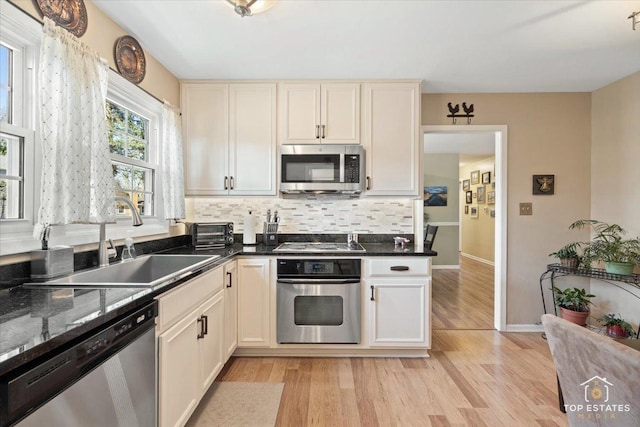 kitchen featuring backsplash, a toaster, light wood-type flooring, appliances with stainless steel finishes, and a sink