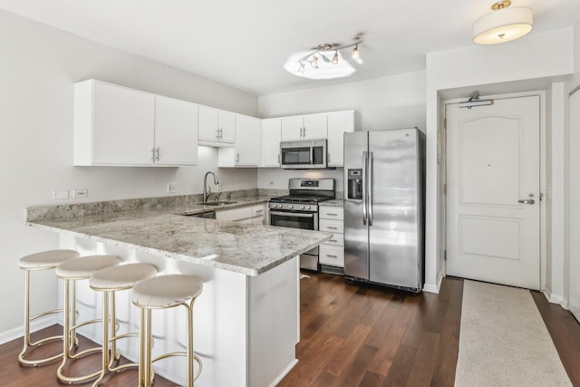 kitchen with dark wood-style floors, appliances with stainless steel finishes, white cabinetry, a sink, and a peninsula