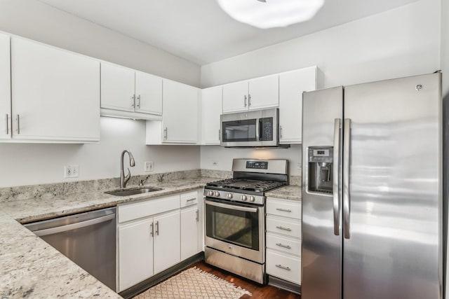 kitchen featuring appliances with stainless steel finishes, dark wood-style flooring, light stone countertops, white cabinetry, and a sink