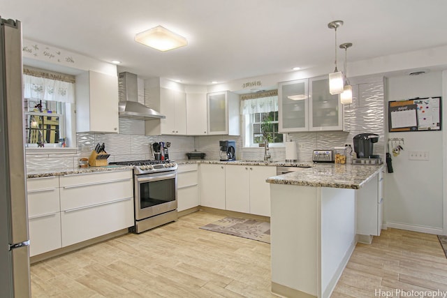 kitchen with decorative backsplash, light wood-style floors, a peninsula, wall chimney range hood, and stainless steel range with gas stovetop